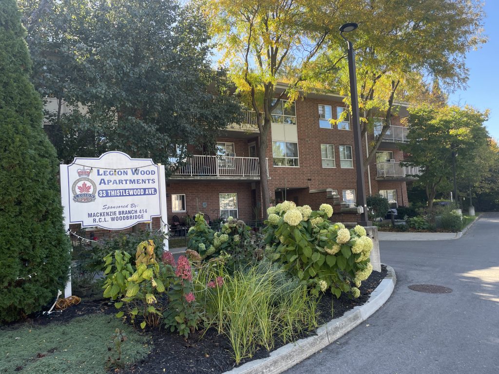 Three storey red brick building with white balconies and surrounded by foliage